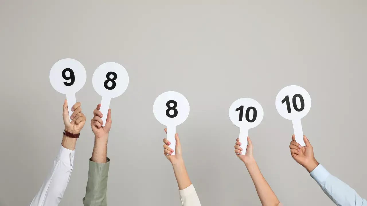 In the image, there are four individuals, each holding up a round white sign with a number printed in the center. The numbers visible on the signs are 9, 8, 8, and 10