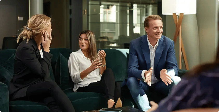 The image shows a group of three people engaged in a conversation in a stylish, modern setting.