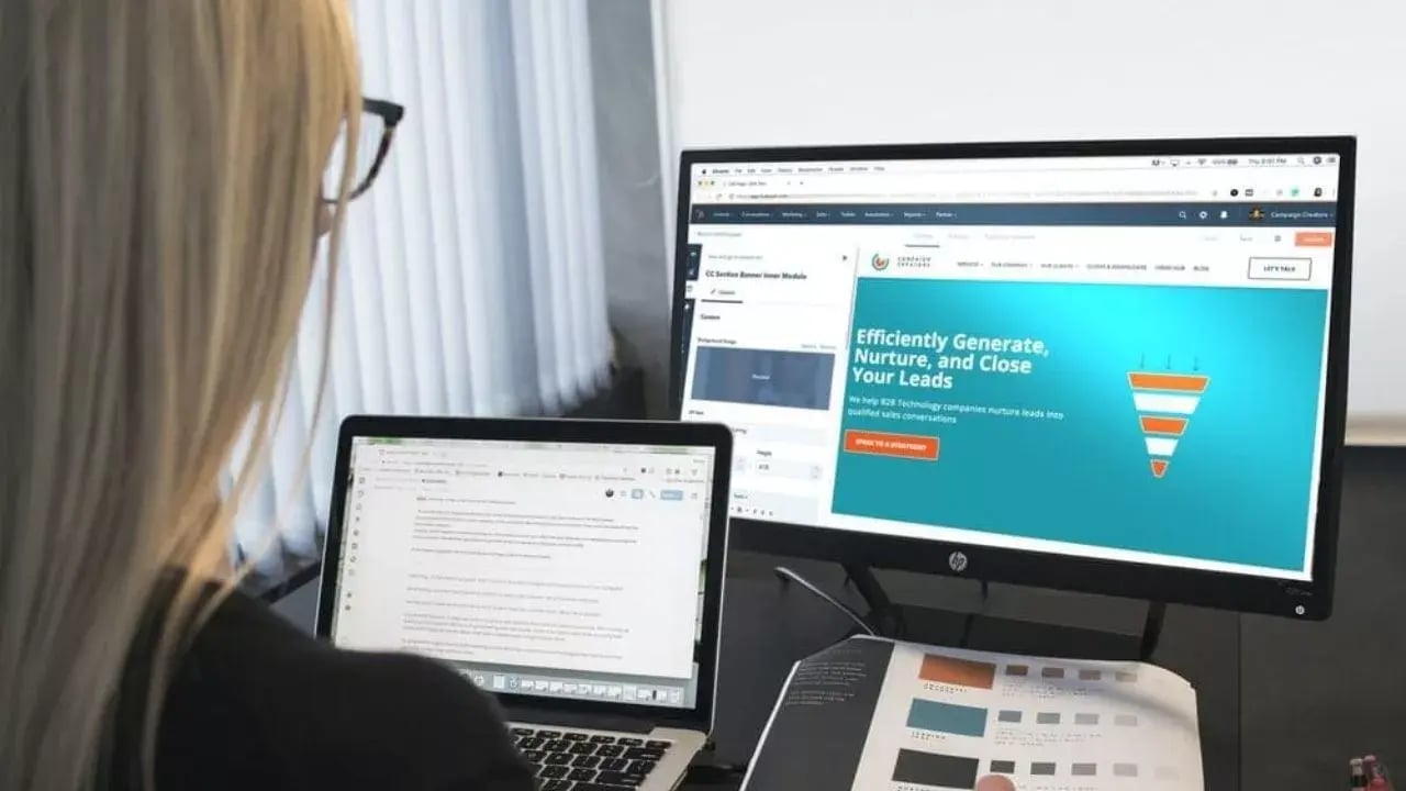 A person working at a laptop and a lager screen