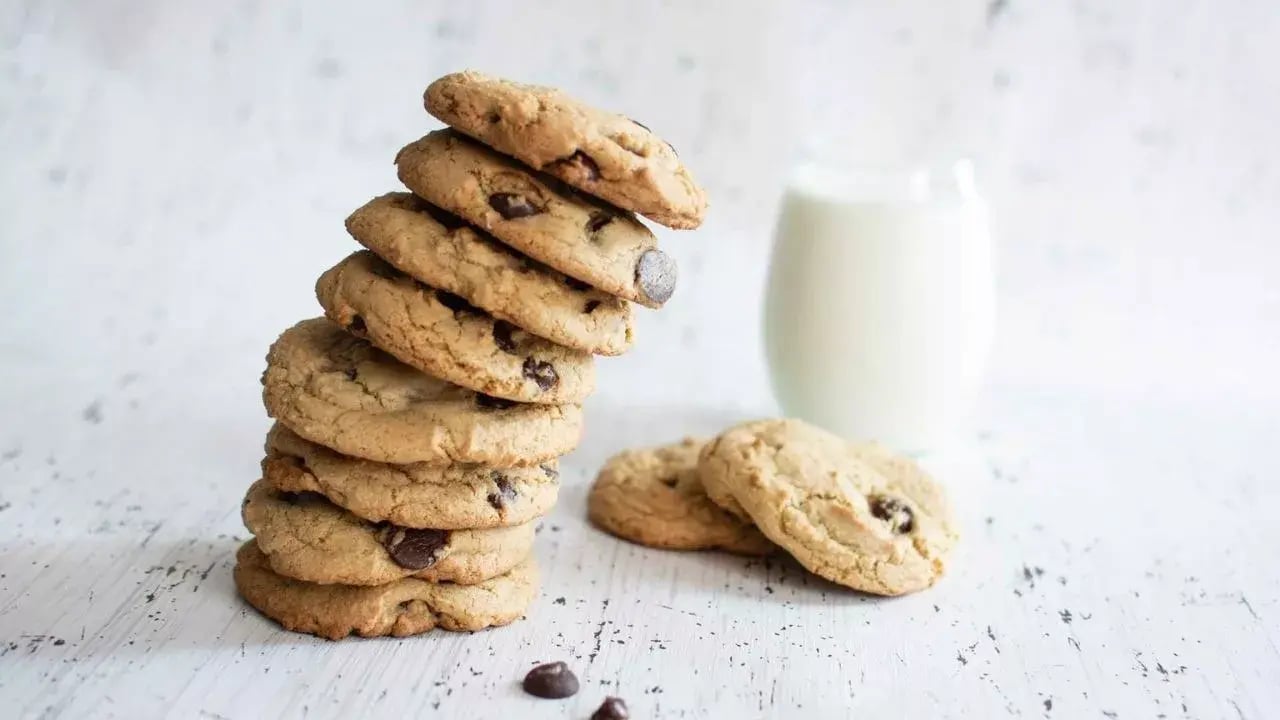 Chocolate chip cookies arranged in a leaning tower formation. Next to the cookies, there is a glass of milk