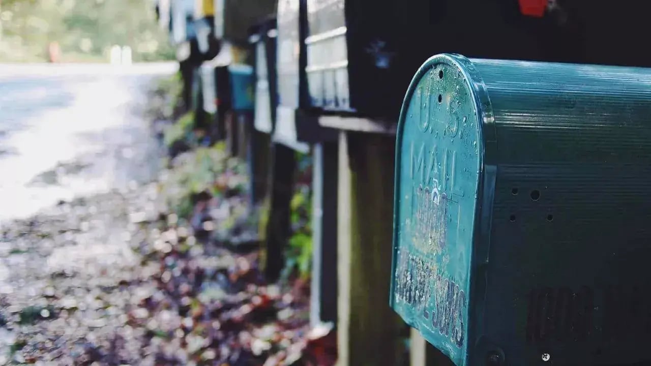 a row of mailboxes along a road, with a focus on a green mailbox in the foreground