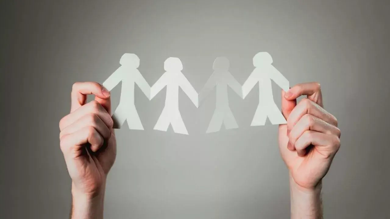 two hands holding a chain of paper cut-out figures, symbolizing unity and connection among people