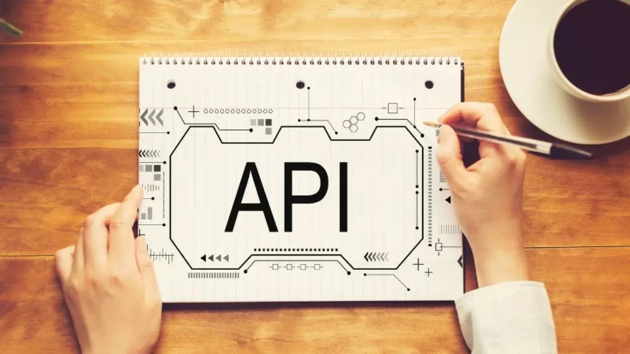 The image features a notebook with a hand holding a pen, drawing a design that prominently displays the letters 