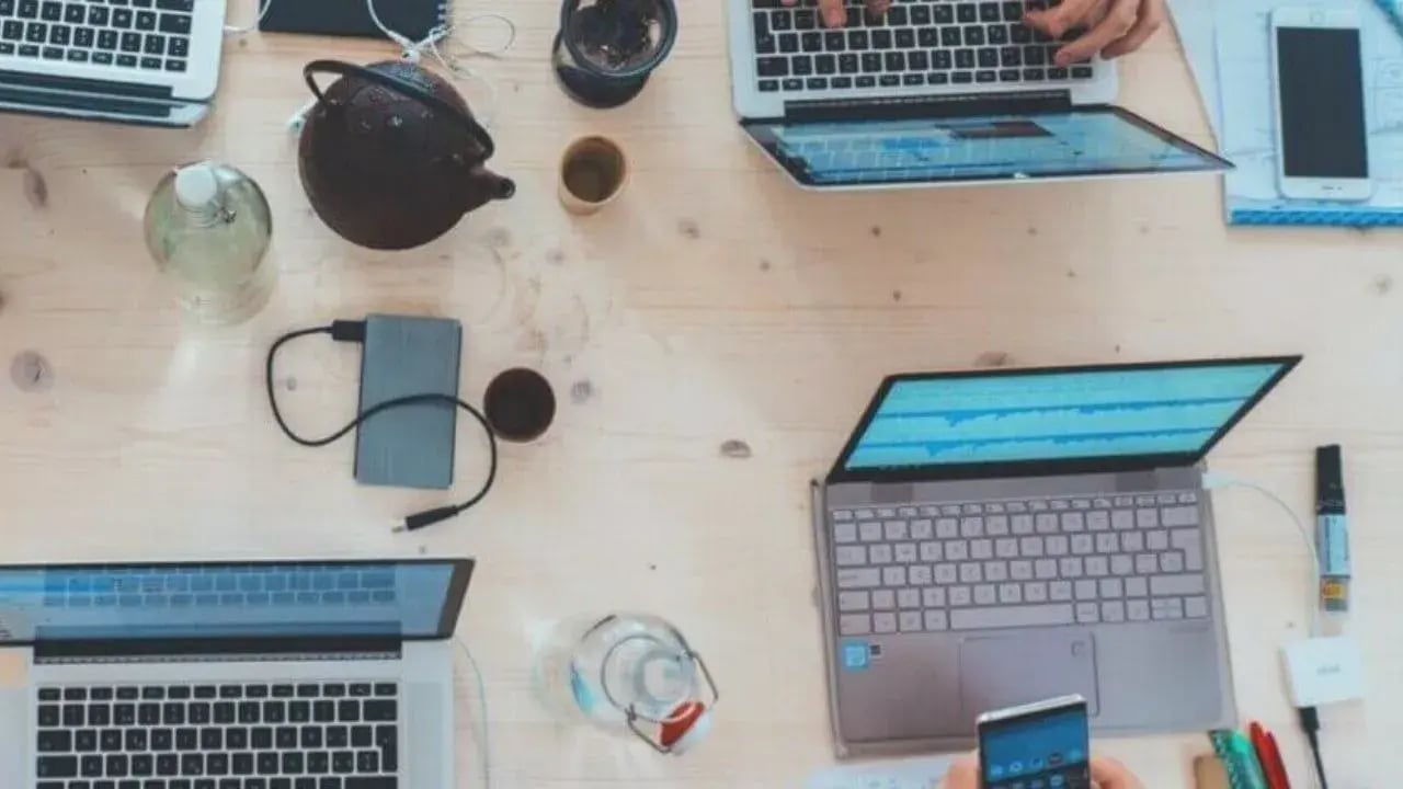 a&nbsp; workspace several laptops, smartphones, a coffee cup, a bowl of snacks, and a water bottle