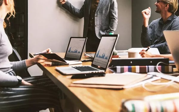 There are three visible individuals, each engaged with their laptops, which display various charts and graphs, suggesting a work-related discussion or presentation.