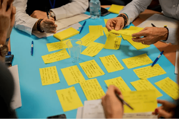 A collaborative work environment where individuals are engaged in an activity that involves yellow sticky notes on a blue table.