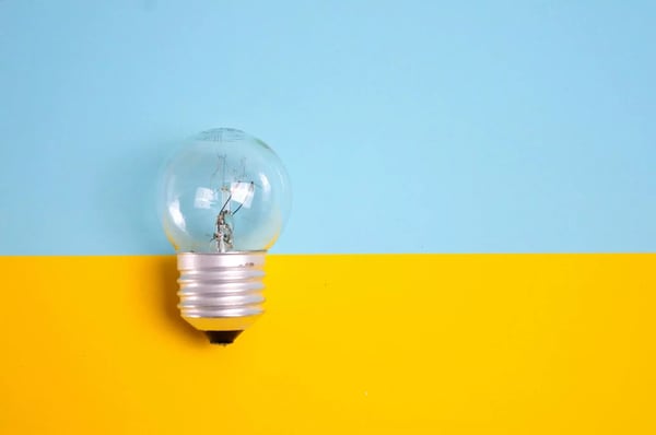 The image shows a single light bulb centered on a bright yellow and blue background that is divided diagonally.